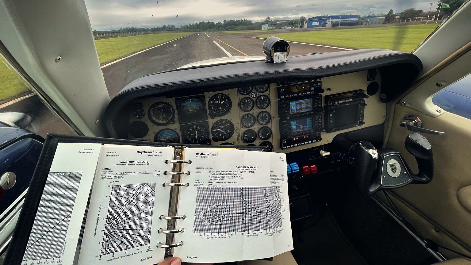 Manual de performance aberto diante do painel de um Baron, com a pista à frente pelo para-brisa.